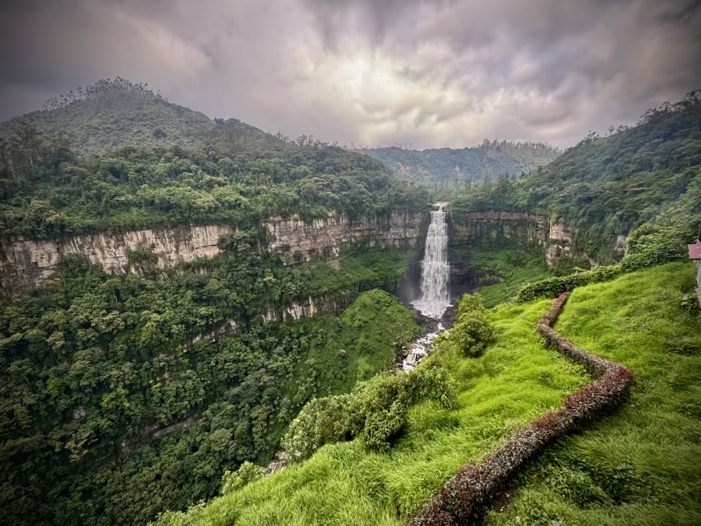 A stunning view of Salto del Tequendama waterfall near Bogotá, Colombia, cascading dramatically into a mist-filled gorge, surrounded by lush green cliffs under a clear blue sky.
